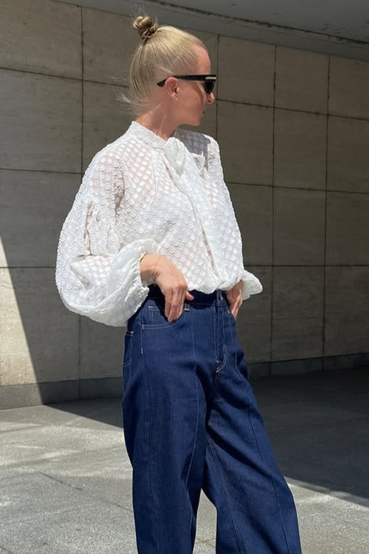 Front view of a white blouse with a textured dot pattern and tie neck