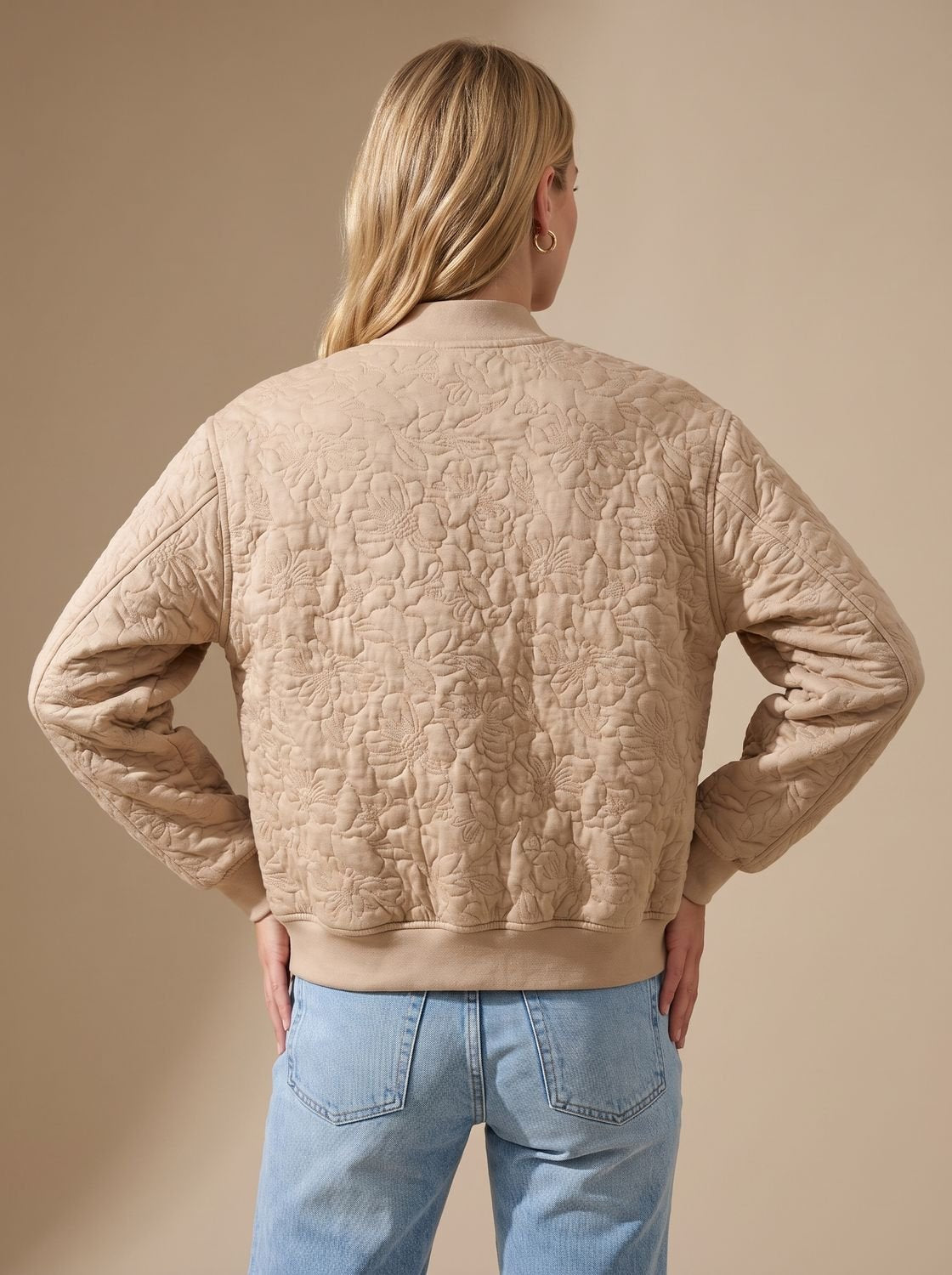 Beige women's quilted bomber jacket shown from the back with ribbed trim